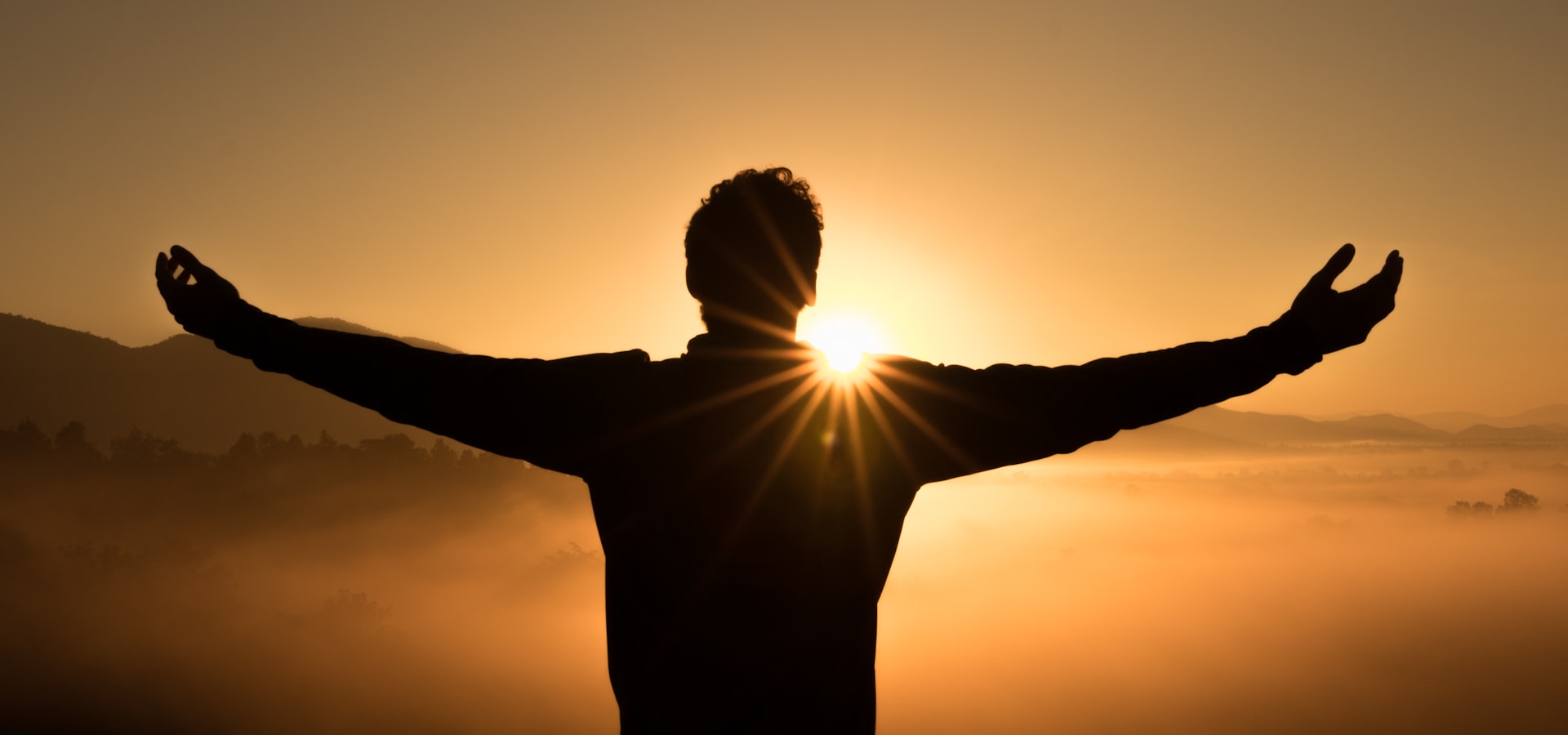 Silhouet met wijd open armen voor de opkomende zon